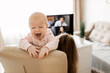 © shunevich - Young woman working at desk at home with computer holding crying tired infant baby holding business meeting at home, online pediatric consultation, chatting with grandparents, mothers forum concept