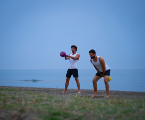 couple of athletes exercising on the beach with kettle bells