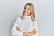 Beautiful blonde woman wearing casual turtleneck sweater happy face smiling with crossed arms looking at the camera. positive person.