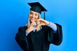 © Krakenimages.com - Beautiful blonde woman wearing graduation cap and ceremony robe smiling in love doing heart symbol shape with hands. romantic concept.