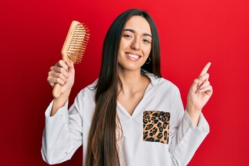 Sticker - Young hispanic girl holding hairbrush smiling happy pointing with hand and finger to the side