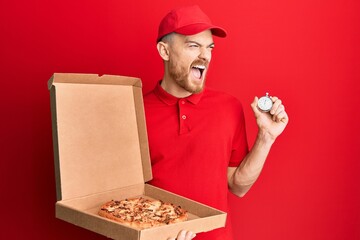 Wall Mural - Young redhead man wearing delivery uniform holding pizza box and countdown clock angry and mad screaming frustrated and furious, shouting with anger. rage and aggressive concept.