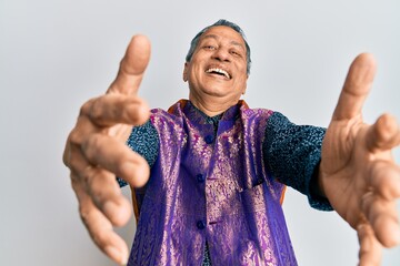 Poster - Middle age indian man wearing traditional indian clothes looking at the camera smiling with open arms for hug. cheerful expression embracing happiness.