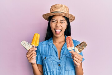 Sticker - Young chinese woman wearing summer style holding ice cream sticking tongue out happy with funny expression.