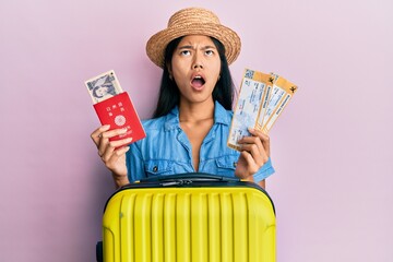 Poster - Young chinese woman holding boarding pass and passport angry and mad screaming frustrated and furious, shouting with anger looking up.