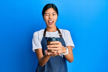 Poster - Young chinese woman wearing waiter apron holding cup of coffee winking looking at the camera with sexy expression, cheerful and happy face.