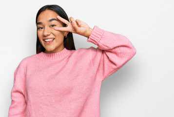 Wall Mural - Young asian woman wearing casual winter sweater doing peace symbol with fingers over face, smiling cheerful showing victory