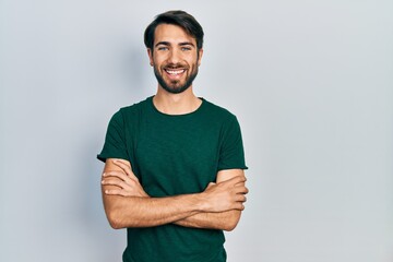 Young hispanic man wearing casual white tshirt happy face smiling with crossed arms looking at the camera. positive person.