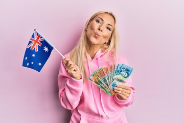 Poster - Young blonde woman holding australian flag and dollars looking at the camera blowing a kiss being lovely and sexy. love expression.