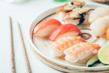 Wall Mural - Set of sushi and maki on plate with soy sauce and chopsticks on white background. Top view with copy space