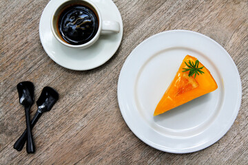 Wall Mural - Top view piece of orange cake in white dish or plate, white cup of dark coffee and spoon on wooden background with copy space. Flat lay of sweet or dessert food on wood table. Snack set for eating.