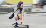 Beautiful happy Asian healthy woman smiling, motion speed riding and playing extreme sportive skateboard as outdoor activity with happiness, relaxation and fun during holidays in summer vacation.