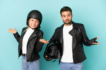 Wall Mural - Couple with motorcycle helmet over isolated blue background having doubts while raising hands and shoulders