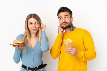 Couple holding hamburger and fried chips over isolated white background thinking an idea while scratching head