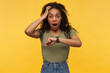 amazed and shocked african american female keeps her hand on head, starring into camera with stressed facial expression. She missed her bus. Isolated over yellow background