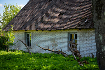 An old abandoned white brick building with a slate roof in an overgrown green meadow. The building has broken wooden windows.