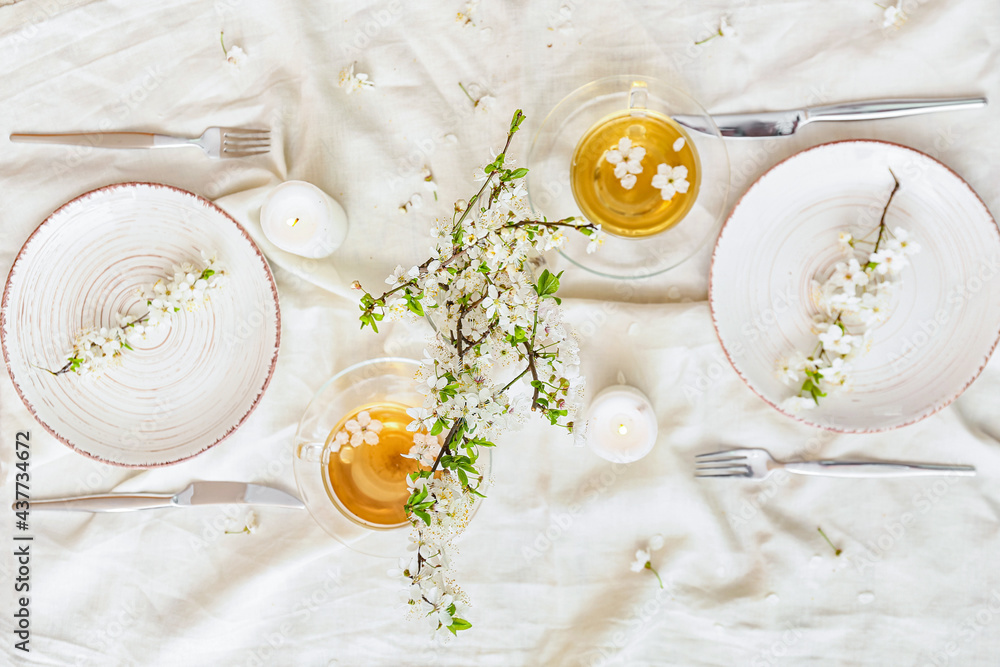Table setting with blooming branches and cups of tea on light background
