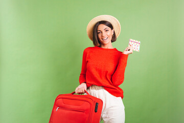 Woman in red casual sweater on green background in straw hat hold suitcase going to vacation cheerful happy excited think where to fly