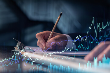 Wall Mural - A trader in formal wear writing down some ideas to research stock market to proceed right investment solutions. Wealth management concept. Hologram Forex chart over close up shot.