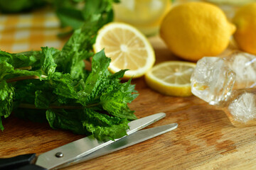 Fresh ripe lemons, peper mint and ice cubes on cutting board on wooden background. lemonade sassy water.Summer mood