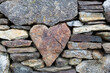 Heart-shaped stone stuck in the middle of a wall with other small and large stones