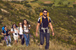© Studio Romantic - Group of smiling young travelers hikers tourists with backpacks hiking with in row in green valley during summer vacations on sunny clear day. Hiking and traveling together, active lifestyle