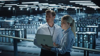 Fototapete - Data Center Female e-Business Enrepreneur and Male IT Specialist talk, Use Laptop. Two Information Technology Professionals on Bridge Overlooking Big Cloud Computing Server Farm. Wide Medium Shot