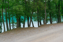Dirt Road Next To The Lake With Turquoise Water Between The Trees