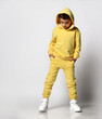 New collection of clothes for children. School boy in bright yellow sportswear and white sneakers on a white background. Cool boy in a hood put his hands in his pockets posing in the studio.