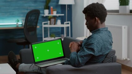 African american man working with chroma key isolated laptop display, green screen mock up mockup computer on black man laps in living room