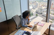 © insta_photos - Serious focused African American businesswoman top manager sitting at desk working typing on laptop computer in modern corporate office near panoramic window. Business technologies concept. Top shot.