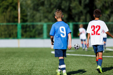 Wall Mural - Young sport boys in blue sportswear running and kicking a  ball on pitch. Soccer youth team plays football in summer. Activities for kids, training	