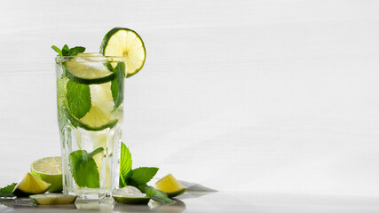 Wall Mural - Fresh homemade mojito cocktail in a tall glass with lime, mint and ice on a white wooden background, copy space