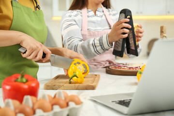 Canvas Print - Mother with adult daughter making dinner while watching online cooking course via laptop in kitchen, closeup