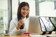 © bongkarn - Female office worker smiling to camera while holding coffee cup and working with laptop