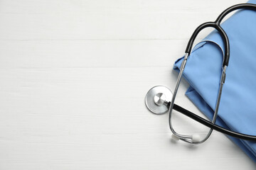 Stethoscope and medical uniform on white wooden background, flat lay. Space for text