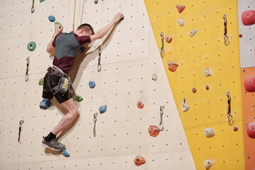 Wall Mural - Disabled man grasping by stones on climbing wall during training in gym