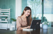 © wattana - Business woman reading information on paperwork and using laptop working on desk.
