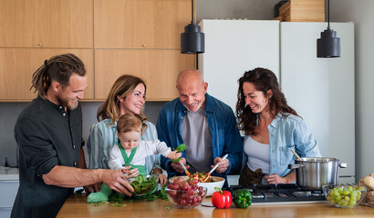 Happy multigeneration family indoors at home preparing vegetable salad.