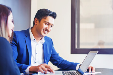 Handsome young Indian professional working on a laptop, training his colleague