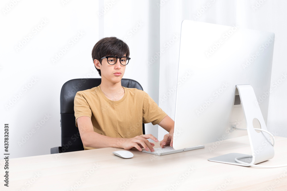Serious teenage boy sitting on the chair while using computer at home ...