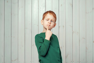 Wall Mural - Ginger little boy 7-9 years old looking sideways with doubtful and skeptical expression