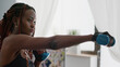 © DC Studio - Athlete black woman wearing sportswear practicing aerobic workout using yoga dumbbells in living room during wellness training. Slim fit adult exercising body muscle enjoying healthy lifestyle
