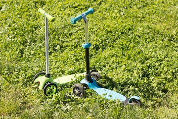 two children's scooters stand on the green grass in the park. children's sports, sports, sports equipment, sports equipment, health, children, urban transport concept