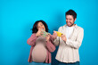 © Roquillo - young couple expecting a baby standing against blue background holding in hands cell playing video games or chatting