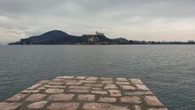 Running Over Arona Jetty With Angera Castle In Background, Fpv Surface Level Pov. Italy