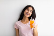 Summer detox and healthy eating concept. Smiling Indian woman with glass of fresh orange juice against white wall