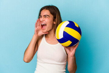 Young caucasian woman playing volleyball isolated on blue background shouting and holding palm near opened mouth.