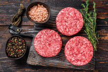 Raw Steak Burgers Patties With Ground Beef And Thyme On A Wooden Cutting Board. Dark Wooden Background. Top View