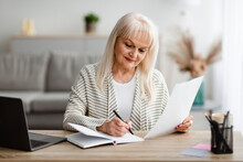 Smiling Mature Woman Writing And Holding Document At Home